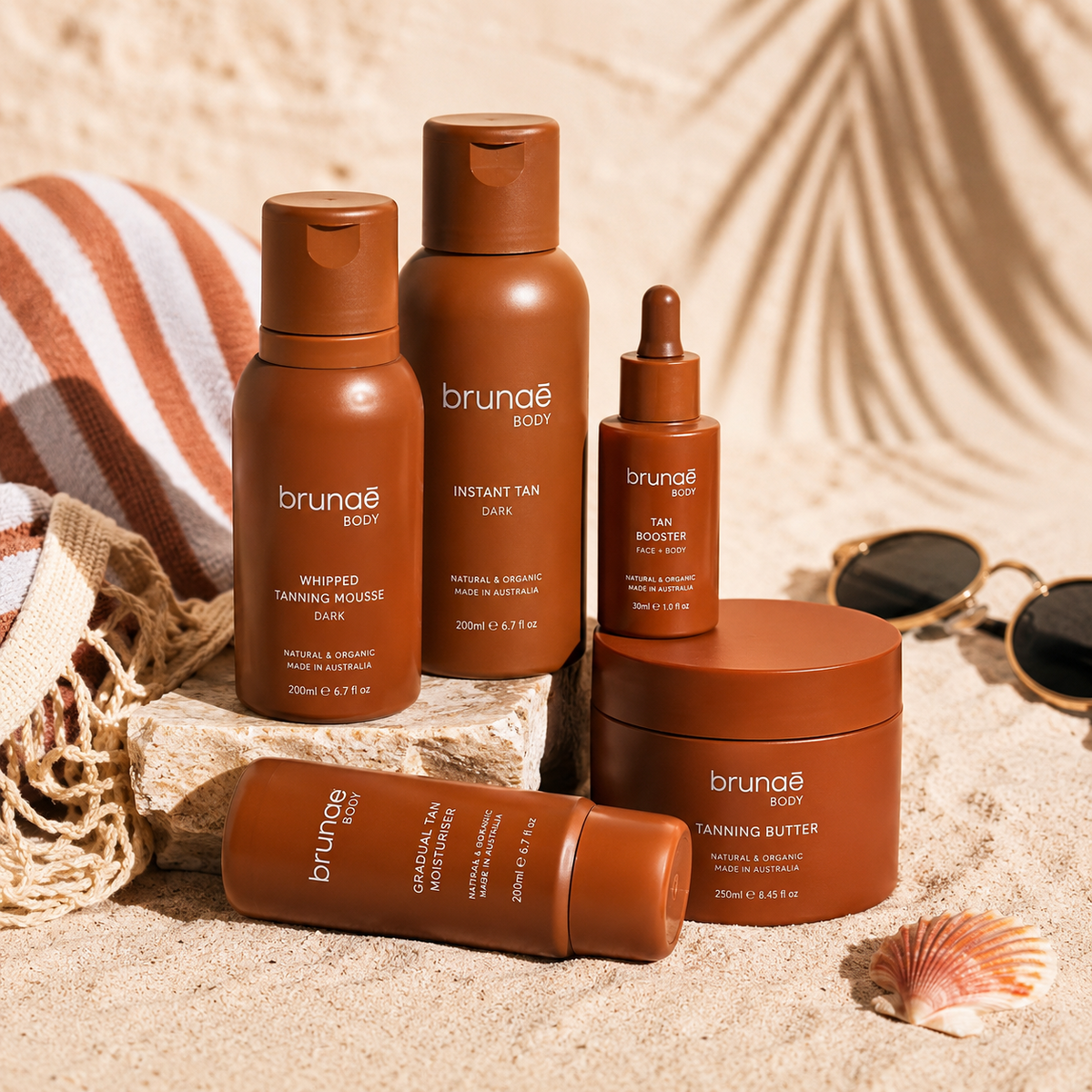 Brunae Body tanning products displayed on a beach with tanning butter, mousse, moisturiser and tanning oil.