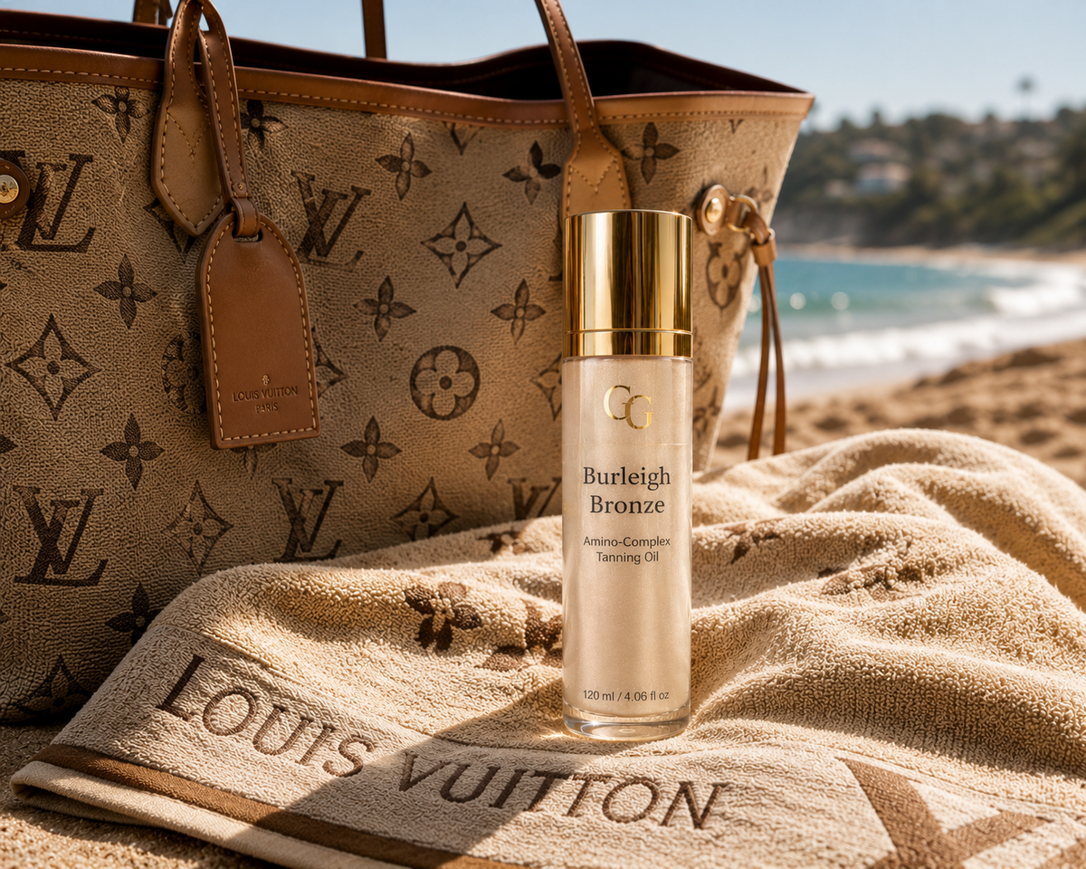 Burleigh Bronze Amino-Complex Tanning Oil beside a luxury designer beach bag and towel on an Australian beach at golden hour.